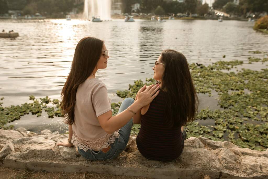 Two women sit by a lake, enjoying a moment of friendship and calm outdoors.